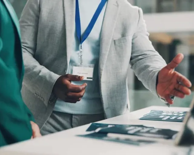 Exhibitor with a lanyard presenting product brochures at a stand
